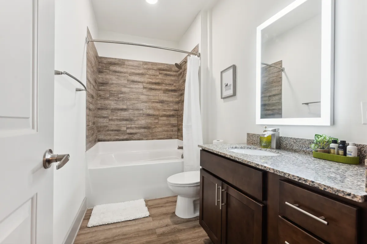 A modern bathroom featuring a deep bathtub, granite countertop, and a large mirror. The calm and refreshing ambiance is ideal for relaxing or starting the day with a self-care routine.