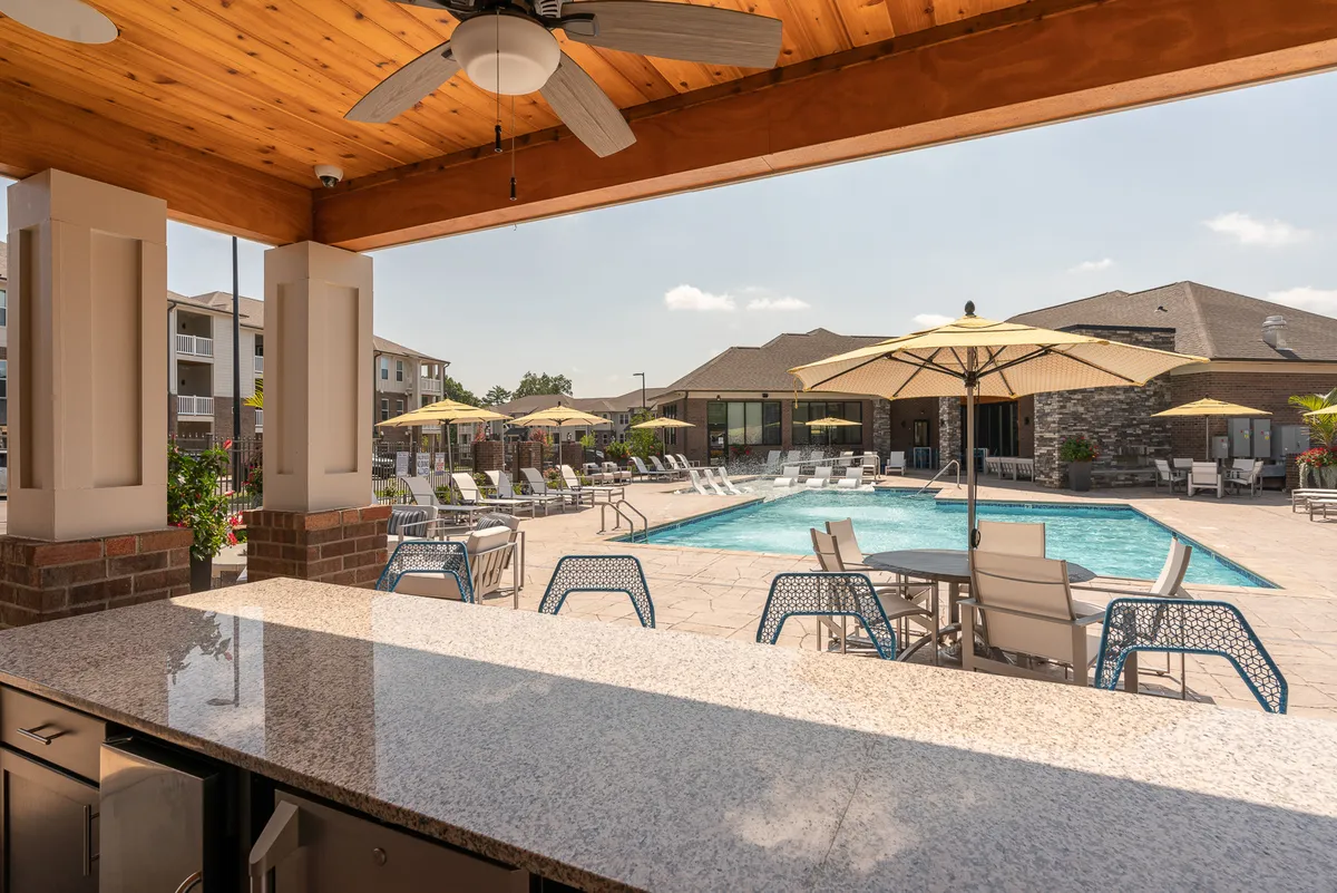 This exterior image showcases a sparkling swimming pool surrounded by comfortable lounge chairs, shaded by large umbrellas. A sleek outdoor bar counter is visible, suggesting a space for refreshing drinks and social gatherings. The scene conveys a relaxed and inviting atmosphere, perfect for unwinding after a night out or sharing a quiet moment together.